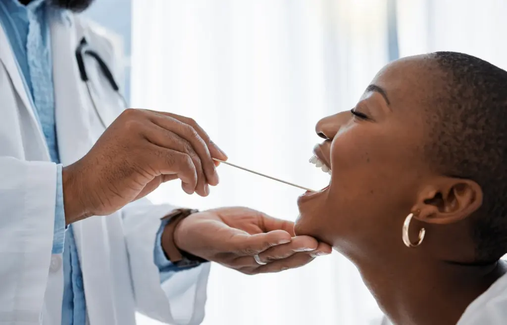 A clinician examining a patient's mouth and throat with a tongue depressor