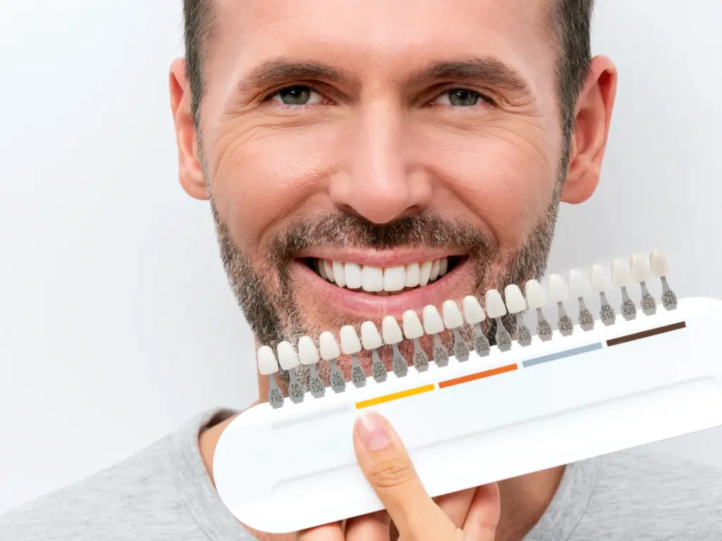 A smiling man holding a tooth whitening shade guide